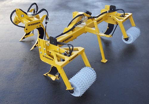 A yellow Mid-Row Ripper and its smaller version on wet asphalt, shanks and spiked rollers showing