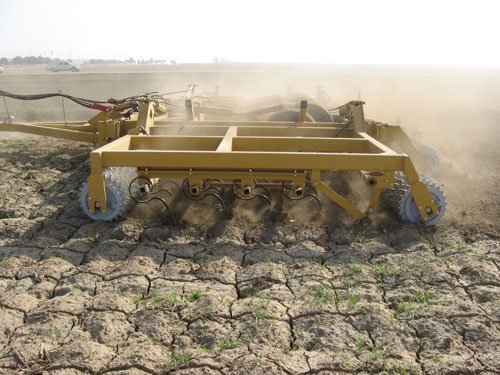 A yellow Folding 4 Bar Till an’ Bedder working cracked dry ground, dust behind it